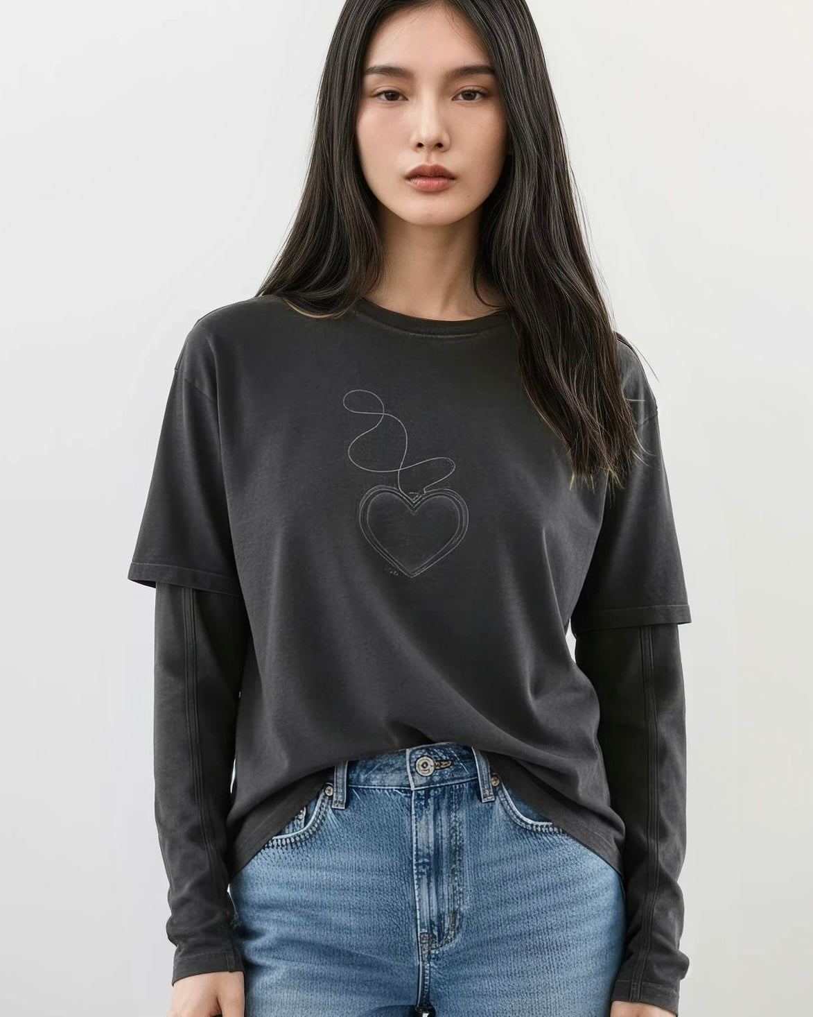 Woman wearing a black faux layered cotton long-sleeve shirt with a heart design and blue jeans on a white background