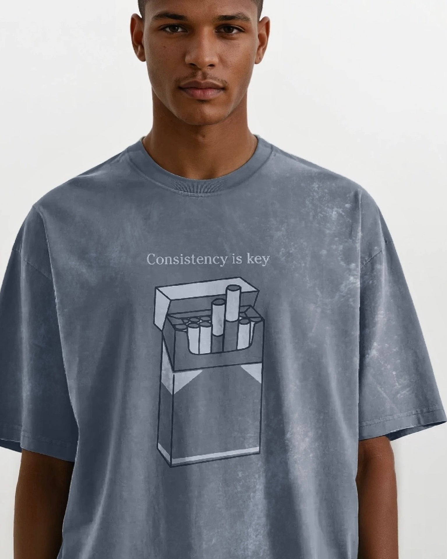 Man wearing an oversized vintage wash gray heavyweight cotton t-shirt with an embroidered graphic design that reads