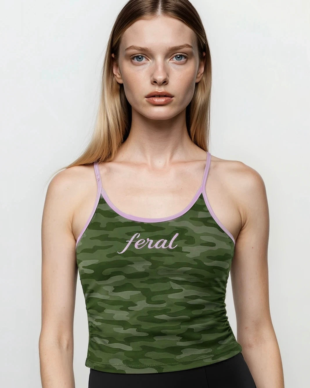 Model wearing a green y2k cami camouflage tank top with 'feral' text on a plain background