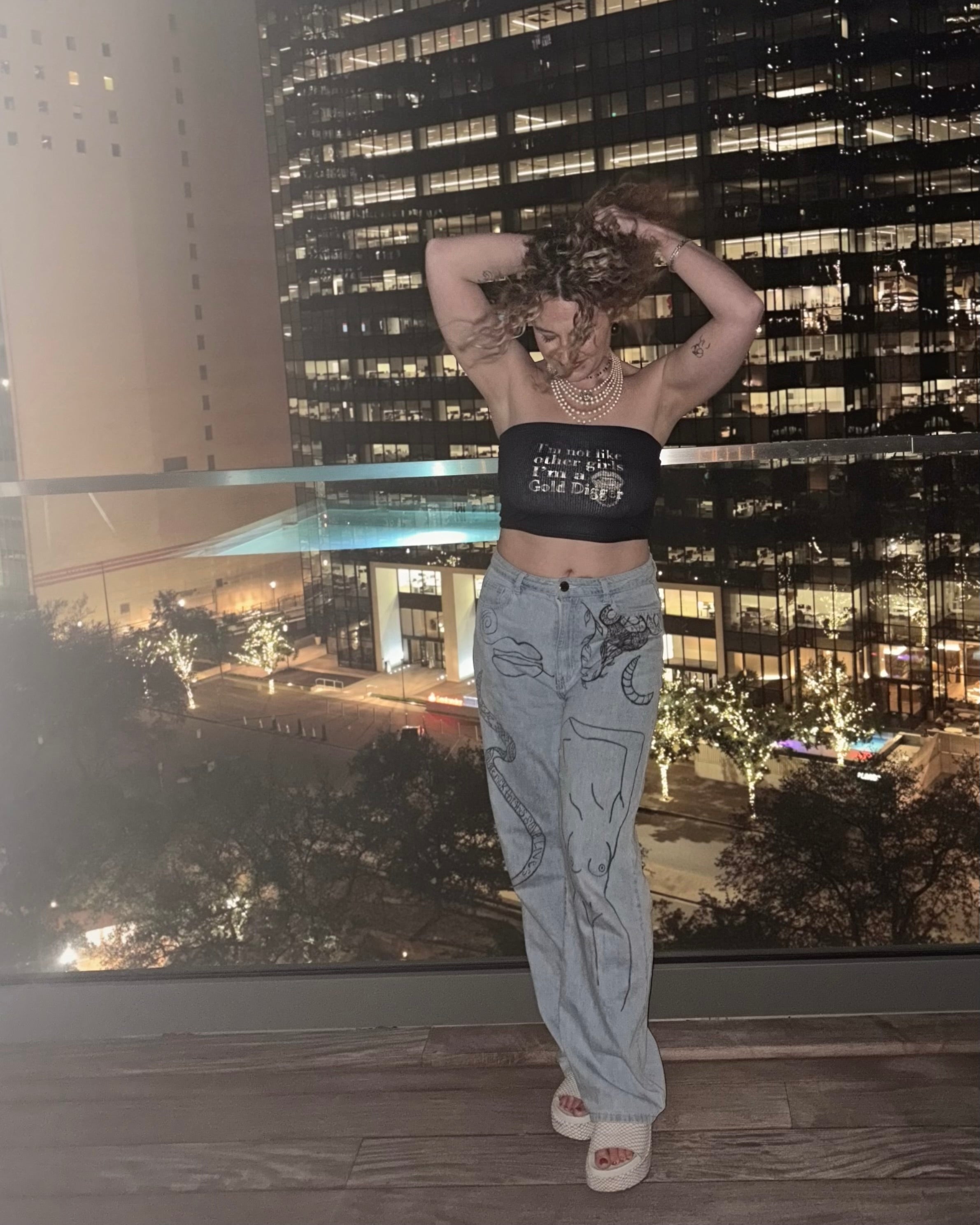 woman wearing jeans and a black strapless ribbed cropped tube top with gold text that reads