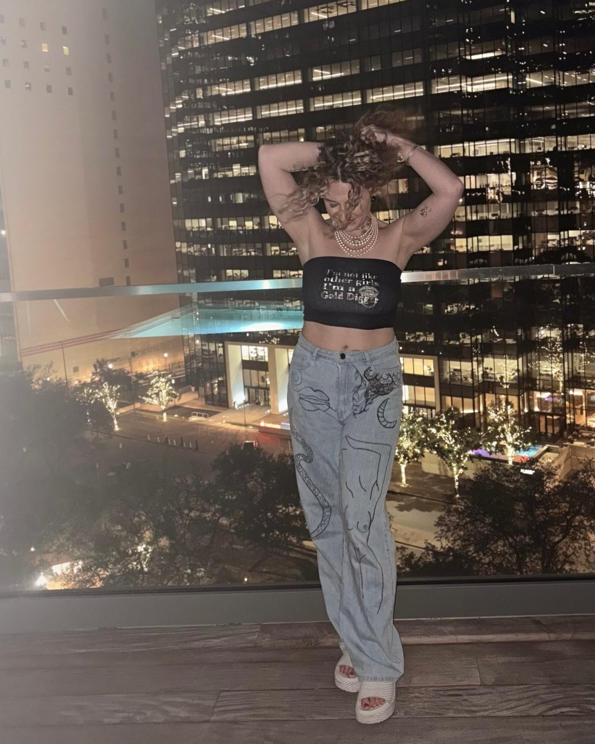 woman wearing jeans and a black strapless ribbed cropped tube top with gold text that reads