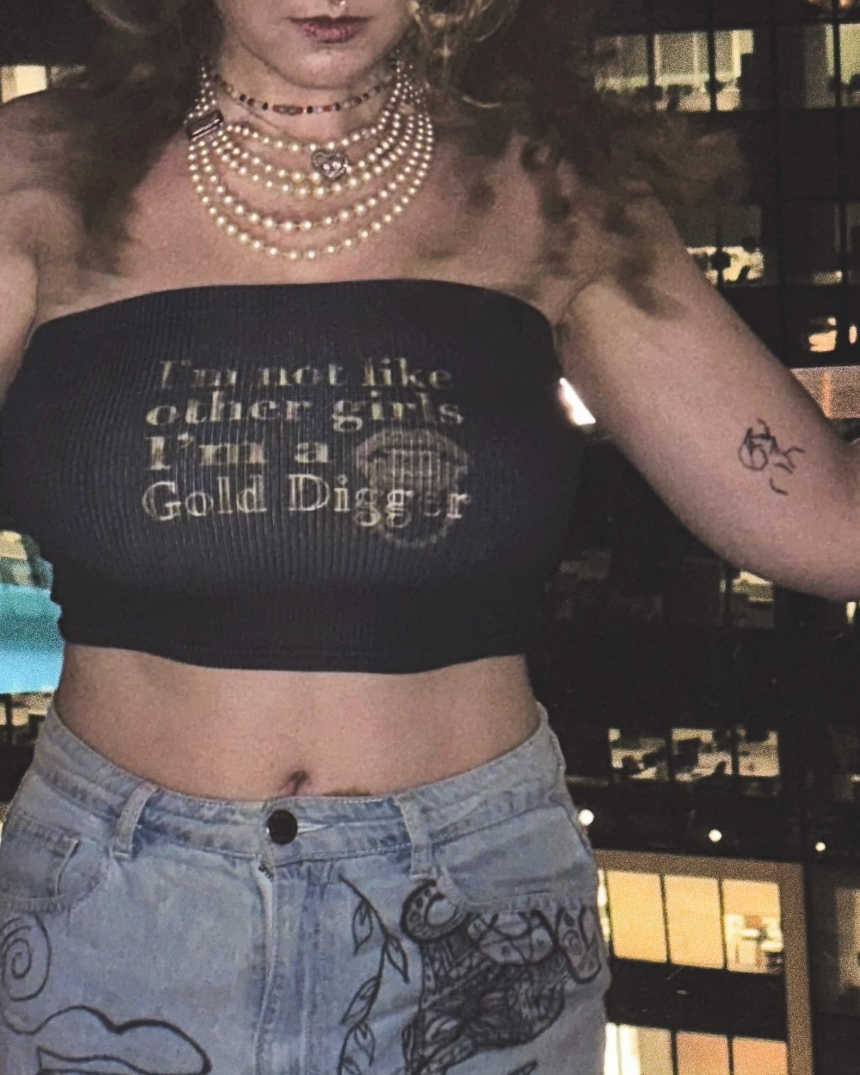 close up view of a woman wearing a black strapless ribbed cropped tube top with gold text that reads