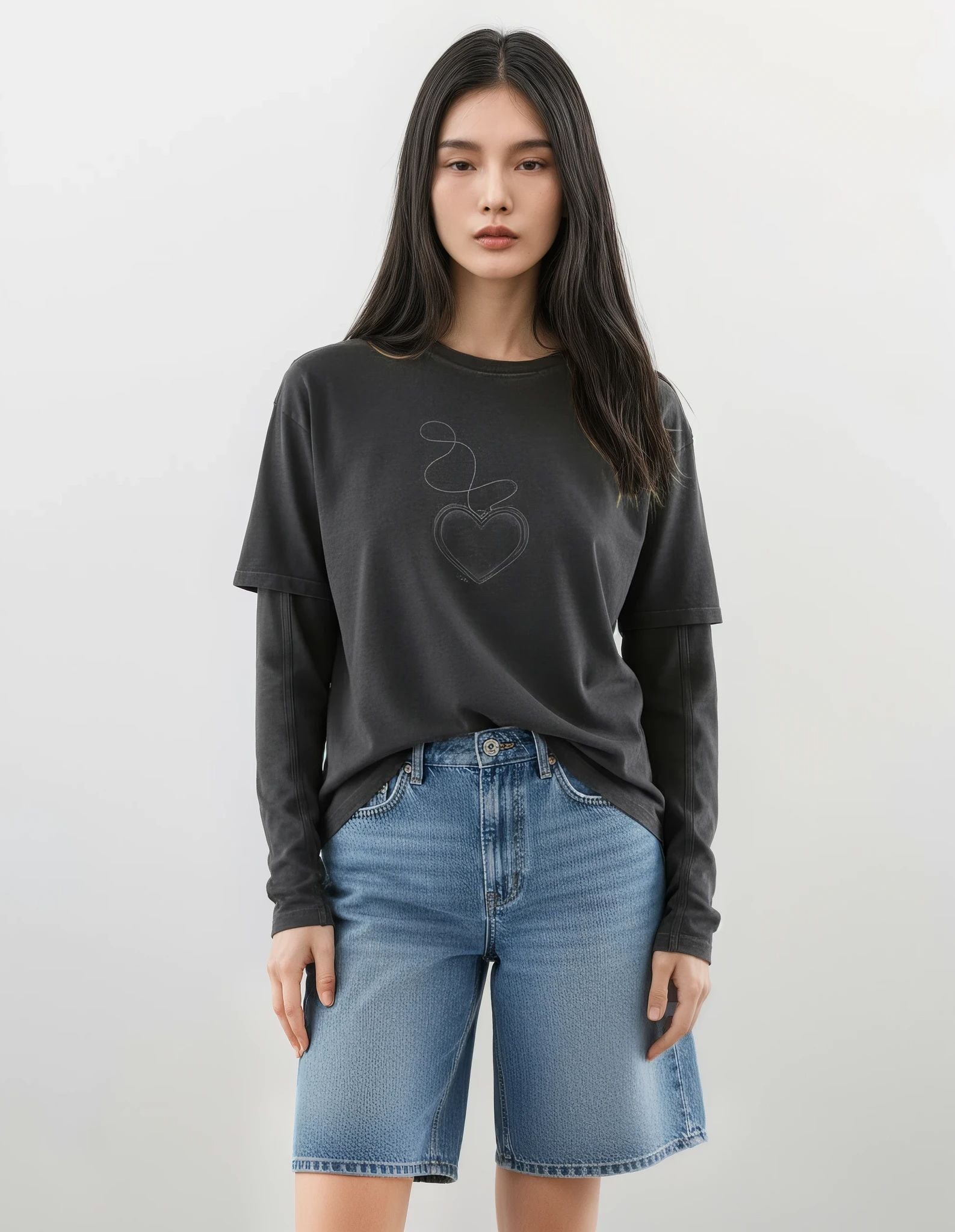 Woman wearing a dark gray long-sleeve shirt with a graphic design of a heart on a chain on a white background