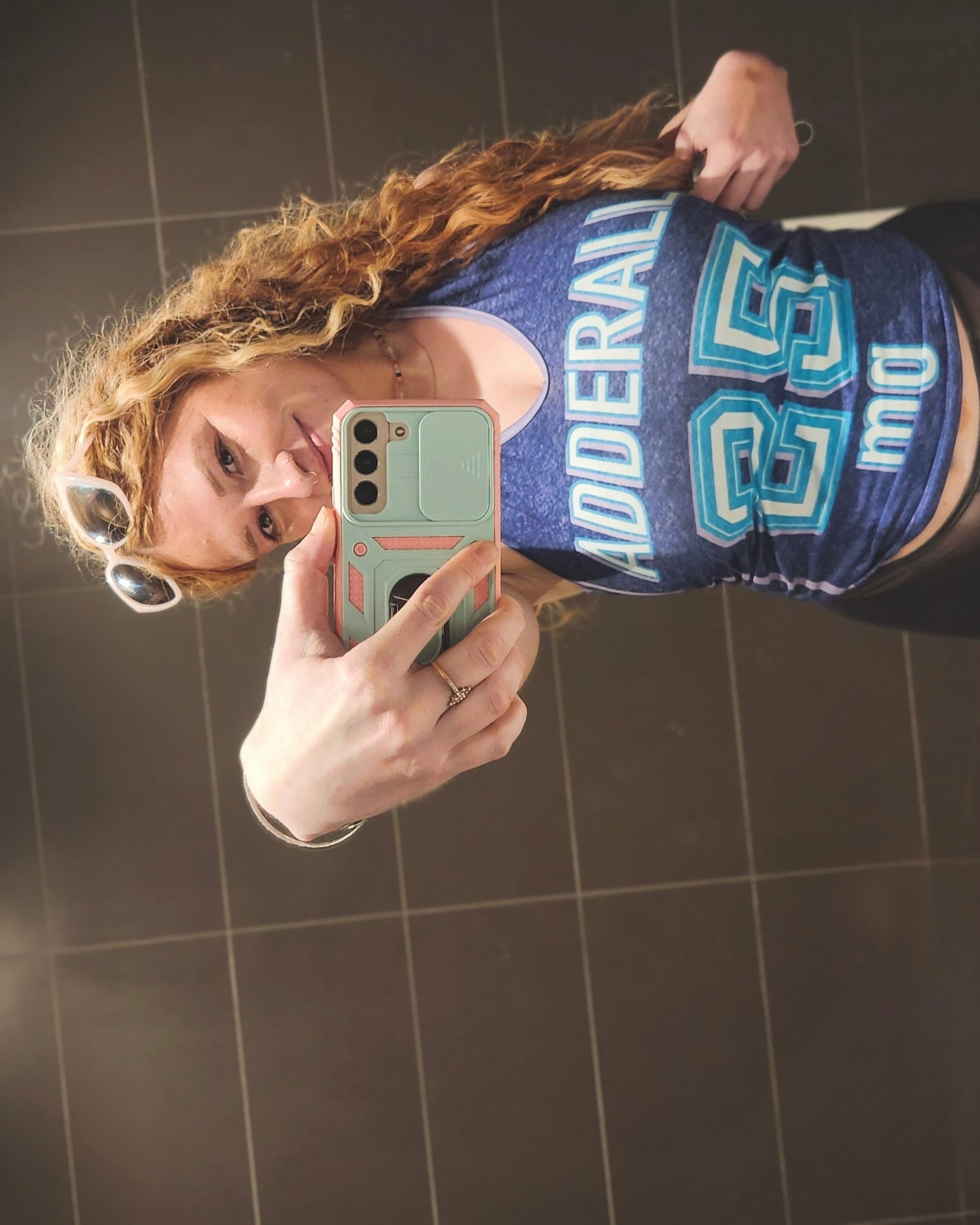 mirror picture of a woman wearing a jersey style dark purple halter top baby tank with light purple trim and contrast stripes with graphic that reads 