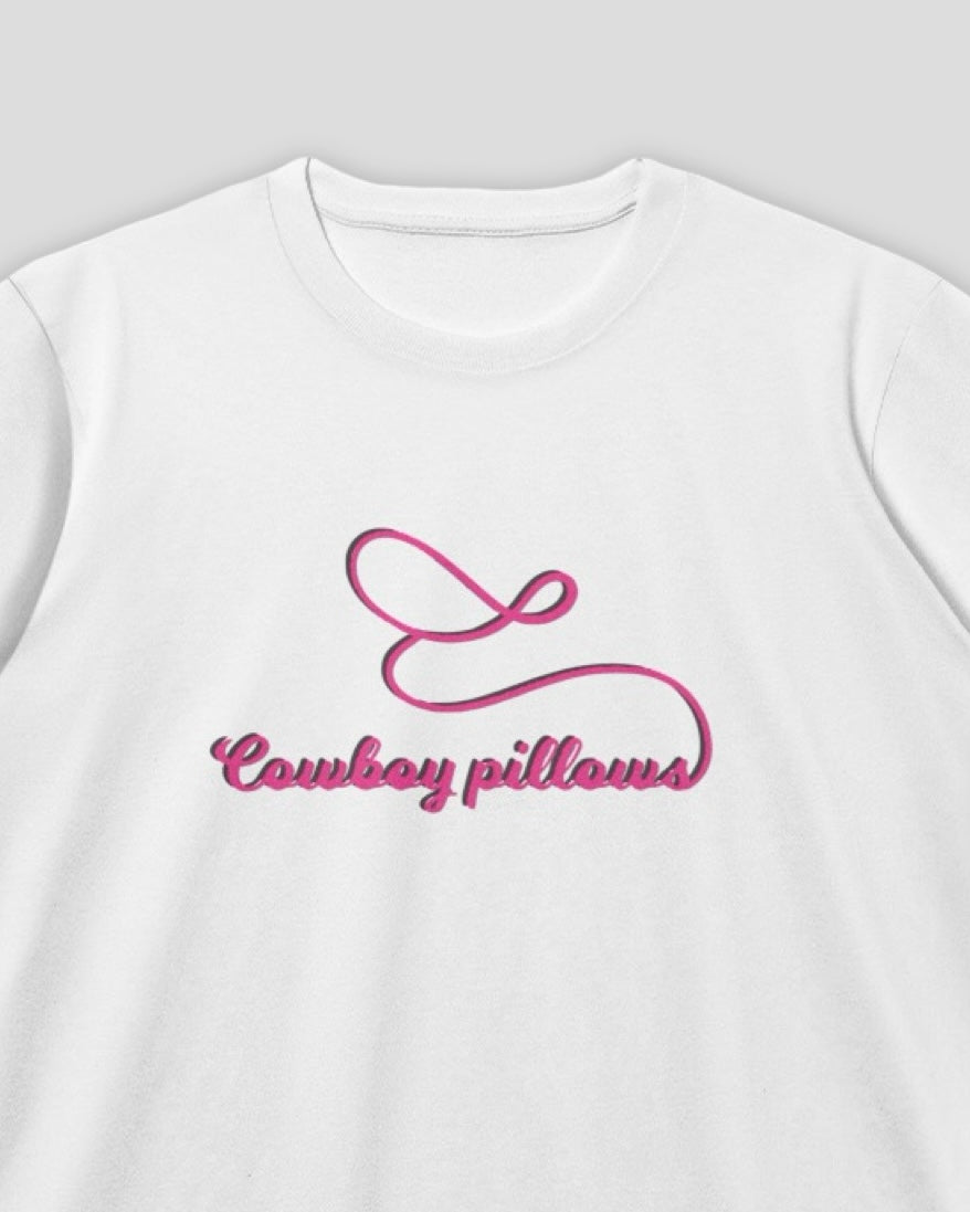 close up of a white cropped fitted crew neck cotton baby tee with embroidered pink text that reads Cowboy Pillows against a white background