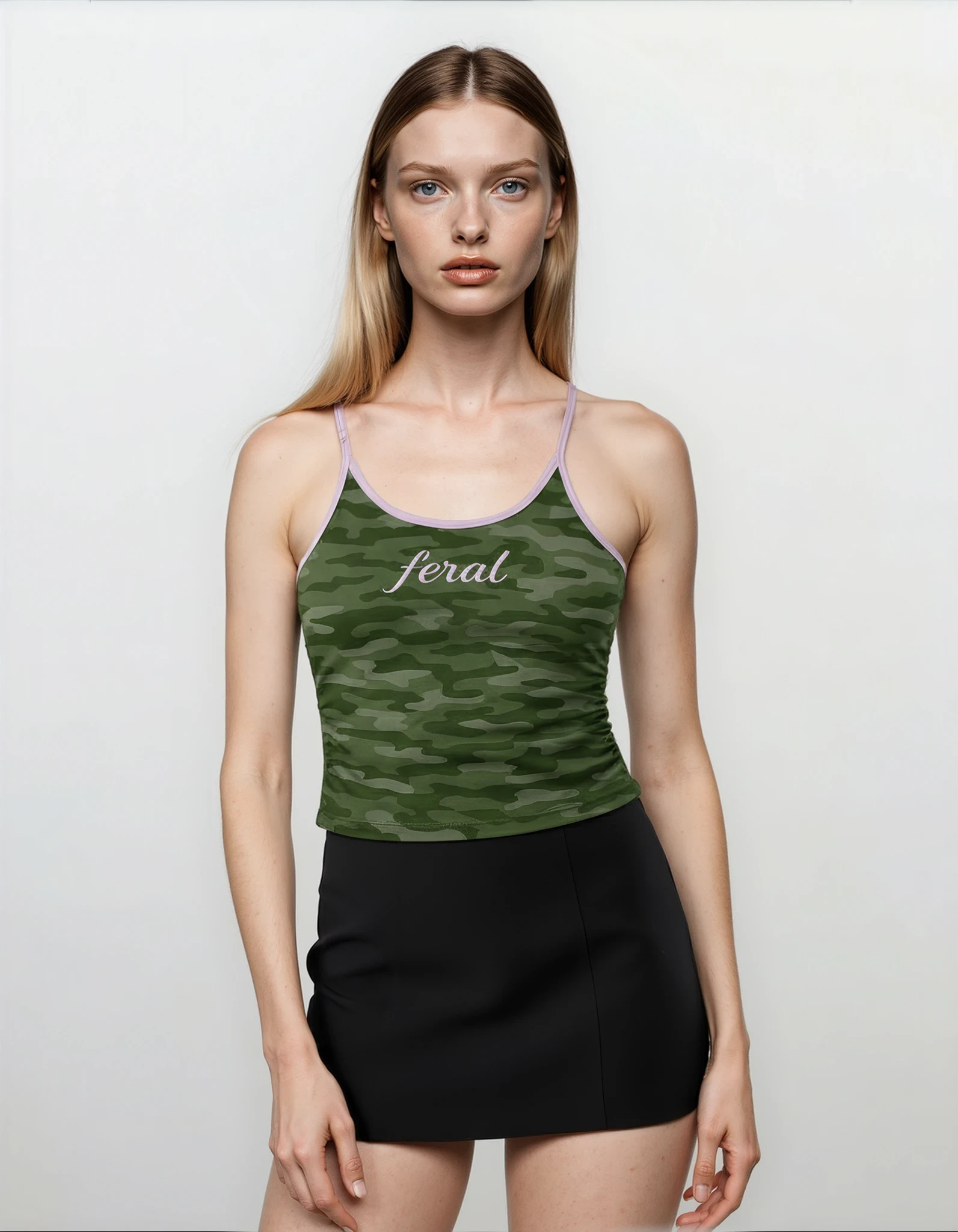 Model wearing a green camouflage y2k cami tank top with 'feral' branding and a black skirt on a white background.