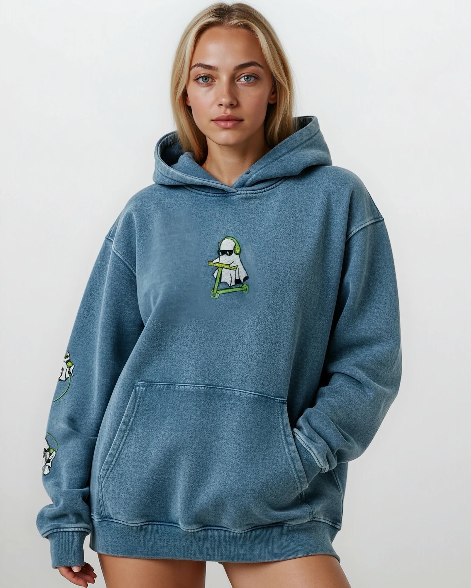woman wearing a denim blue vintage washed heavyweight cotton oversized hoodie with a kangaroo pocked and embroidered original ghost graphics on the front and left arm against a white background