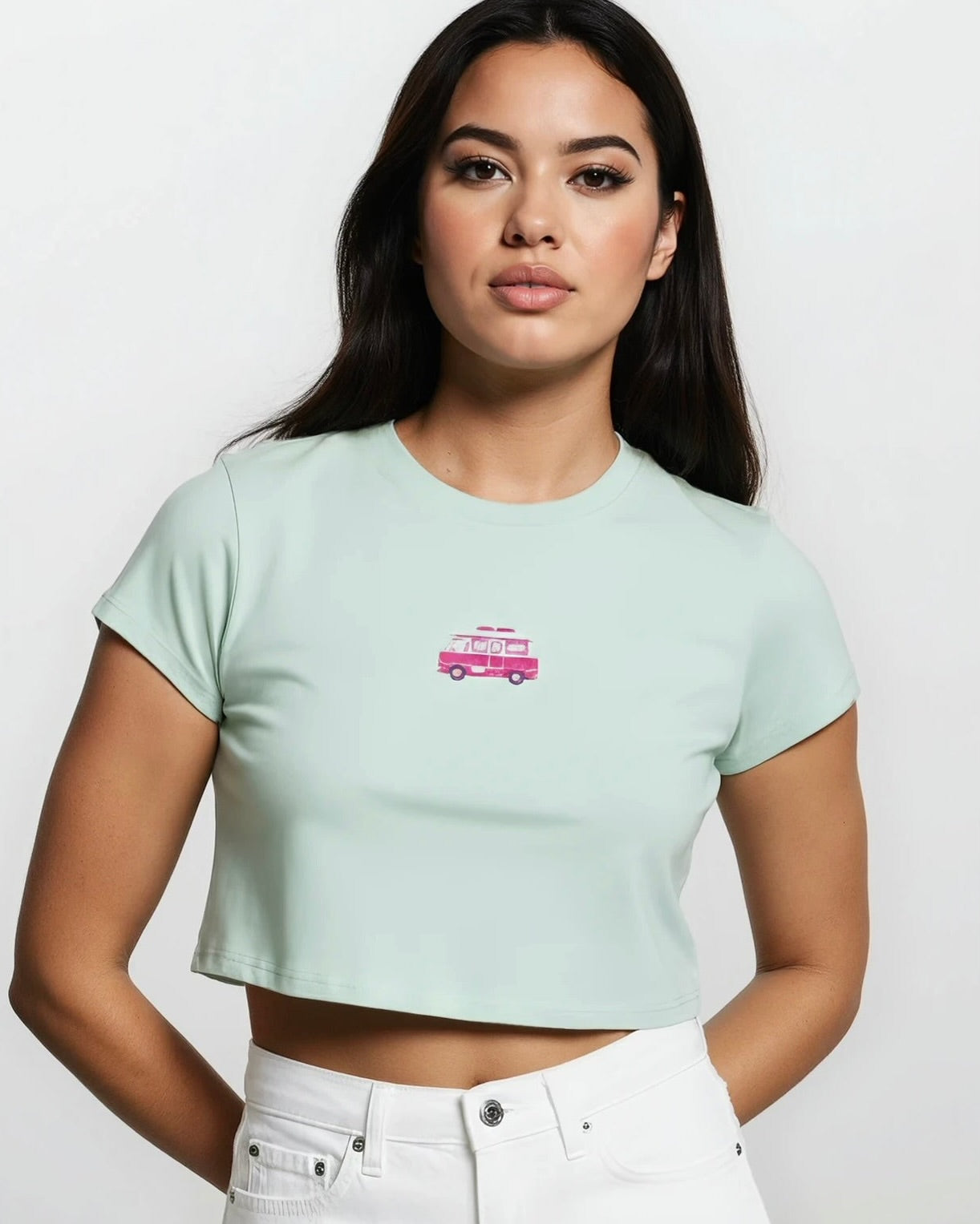 Woman wearing a light blue crop cotton baby tee with an embroidered design of a pink camper van against a white background