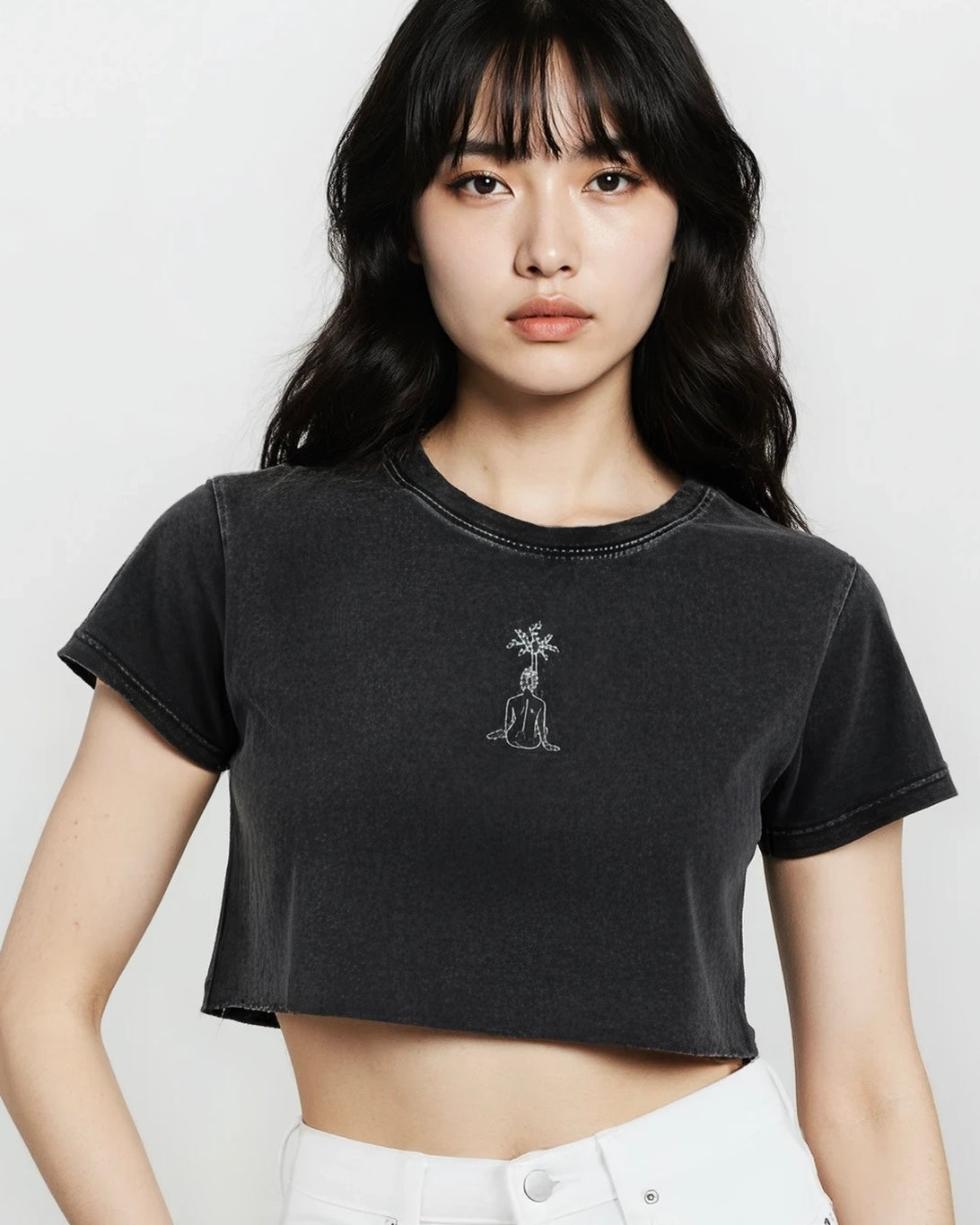 Woman wearing a black crop t-shirt with washed finished and a small embroidery design of a woman, photographed against a white background