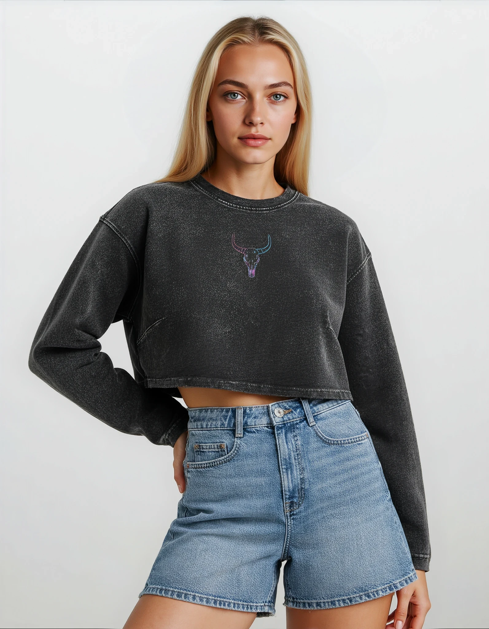 woman wearing a long sleeve faded black cotton raw hem crop top with blue and pink embroidered original longhorn design against a white background