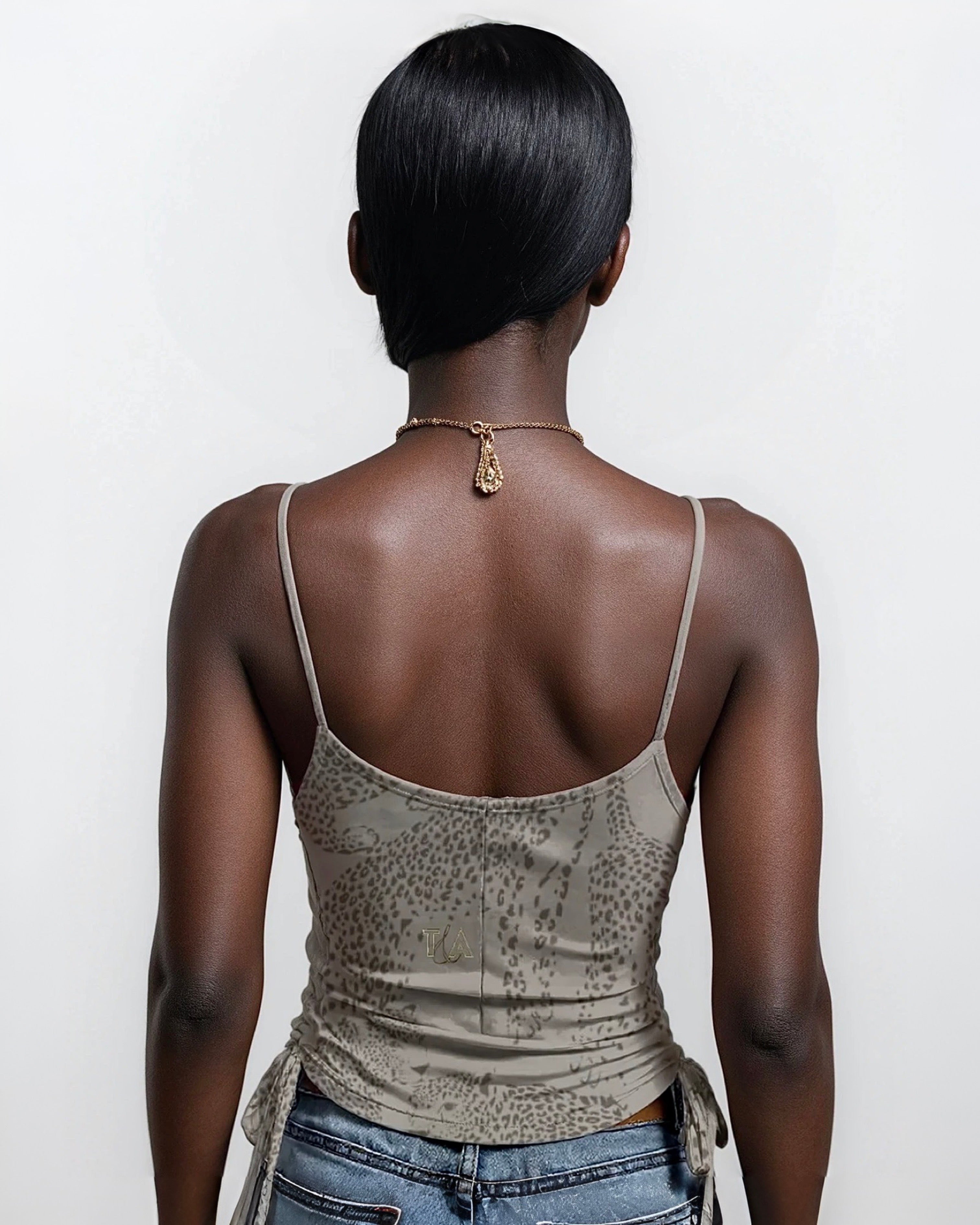 Person wearing a taupe tank top with spaghetti straps and neutral cheetah print on a plain background