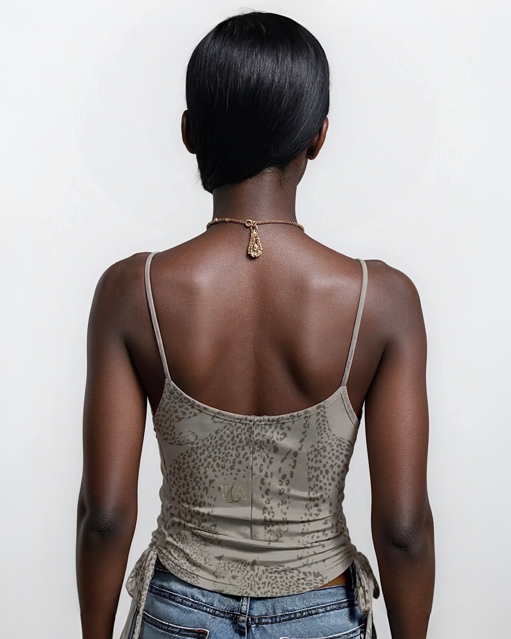Person wearing a taupe tank top with spaghetti straps and neutral cheetah print on a plain background